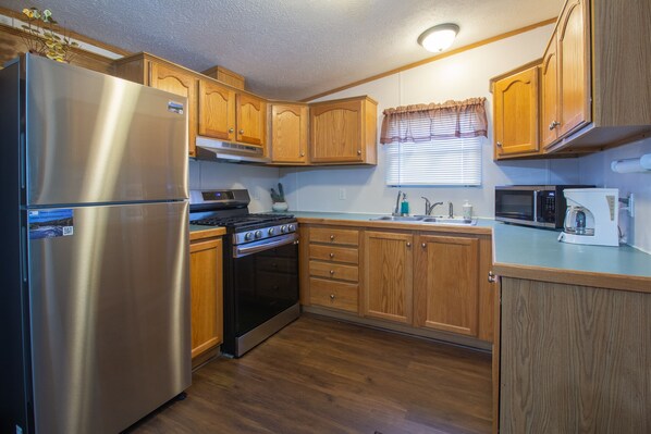 A compact kitchen with wooden cabinets, a stainless steel refrigerator, a stove, and a microwave.