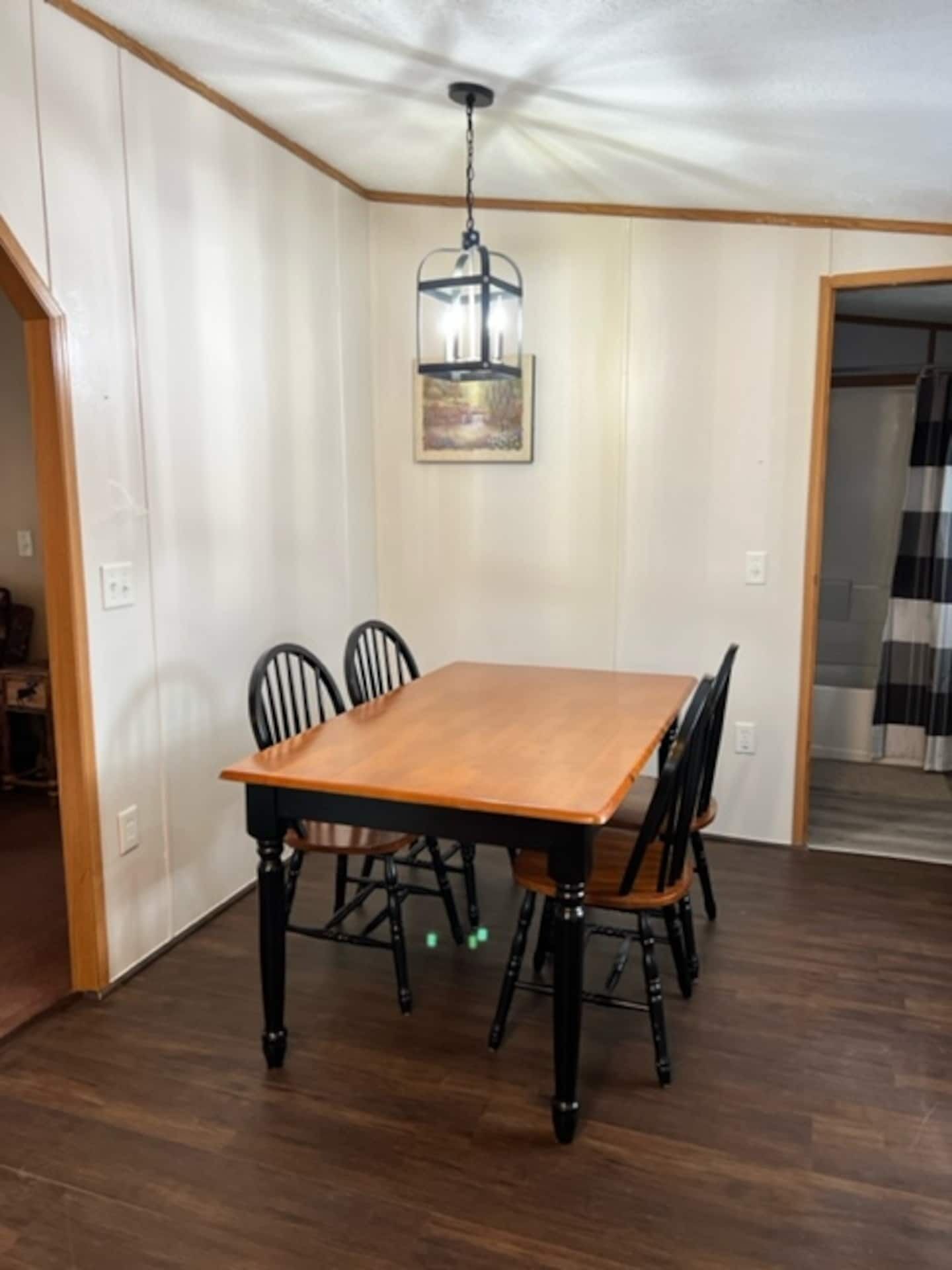 Een eetruimte met een houten tafel en stoelen, een hanglamp en een schilderij aan de muur.