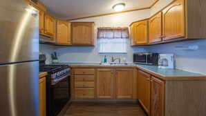 A compact kitchen with wooden cabinets, a stainless steel refrigerator, a stove, a microwave, and a coffee maker. - Stay In Ohiopyle near The Falls & GAP trail. (Ohiopyle)