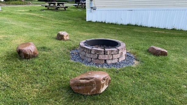 A fire pit surrounded by rocks in a grassy yard with a picnic table and a building in the background. - Stay In Ohiopyle near The Falls & GAP trail. (Ohiopyle)