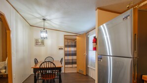 A compact kitchen with a stainless steel refrigerator, wooden dining table, and chairs. - Stay In Ohiopyle near The Falls & GAP trail. (Ohiopyle)