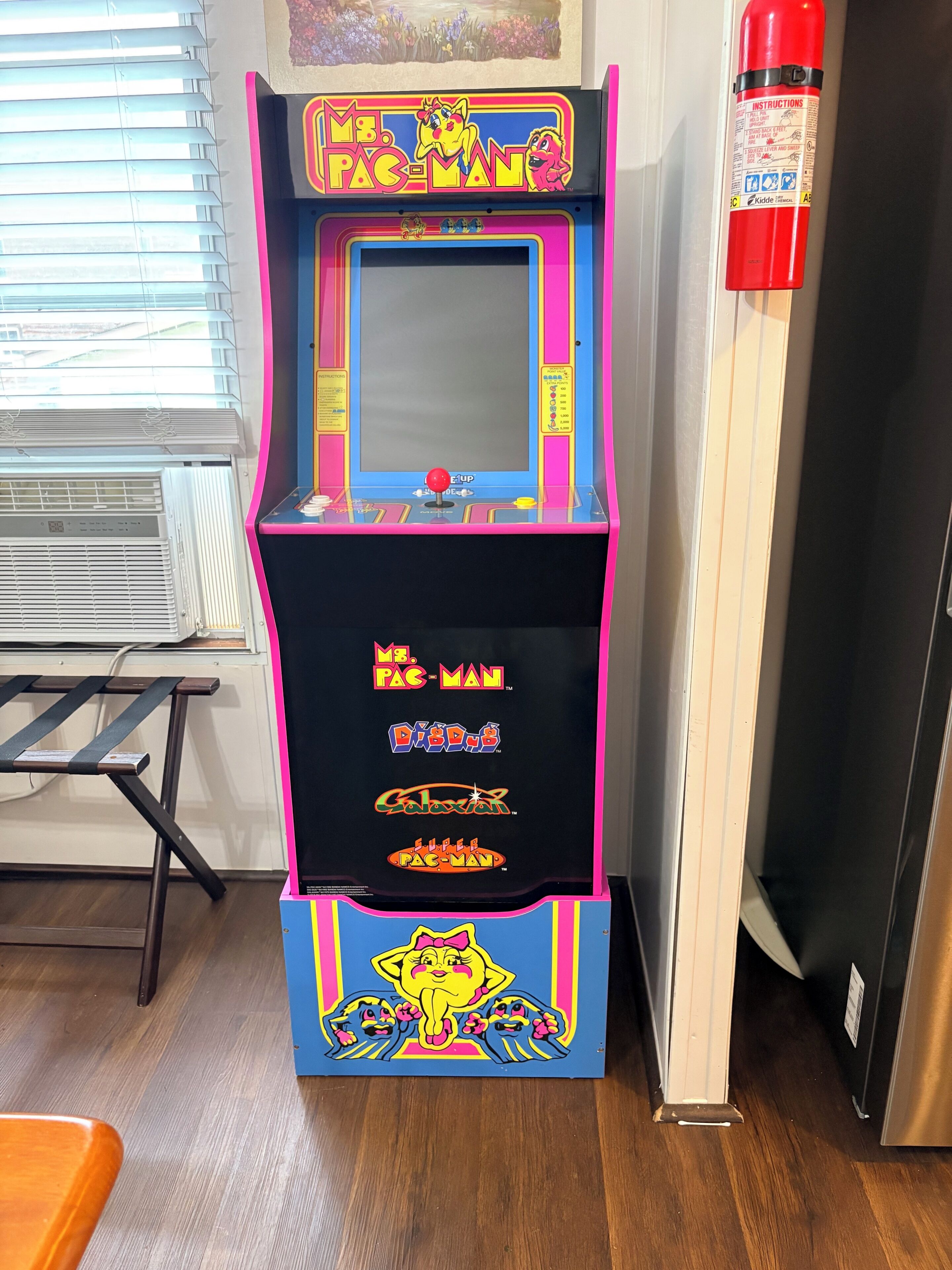 Une borne d’arcade Pac-Man ancienne, avec un extincteur fixé au mur à côté.