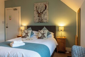 A neatly made bed with a blue blanket, two pillows with deer images, a deer head on the wall, and two bedside lamps. - Morlea Bed & Breakfast (Inverness)