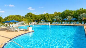 A swimming pool with a clear blue water surface, surrounded by lounge chairs and umbrellas, with a tropical backdrop.