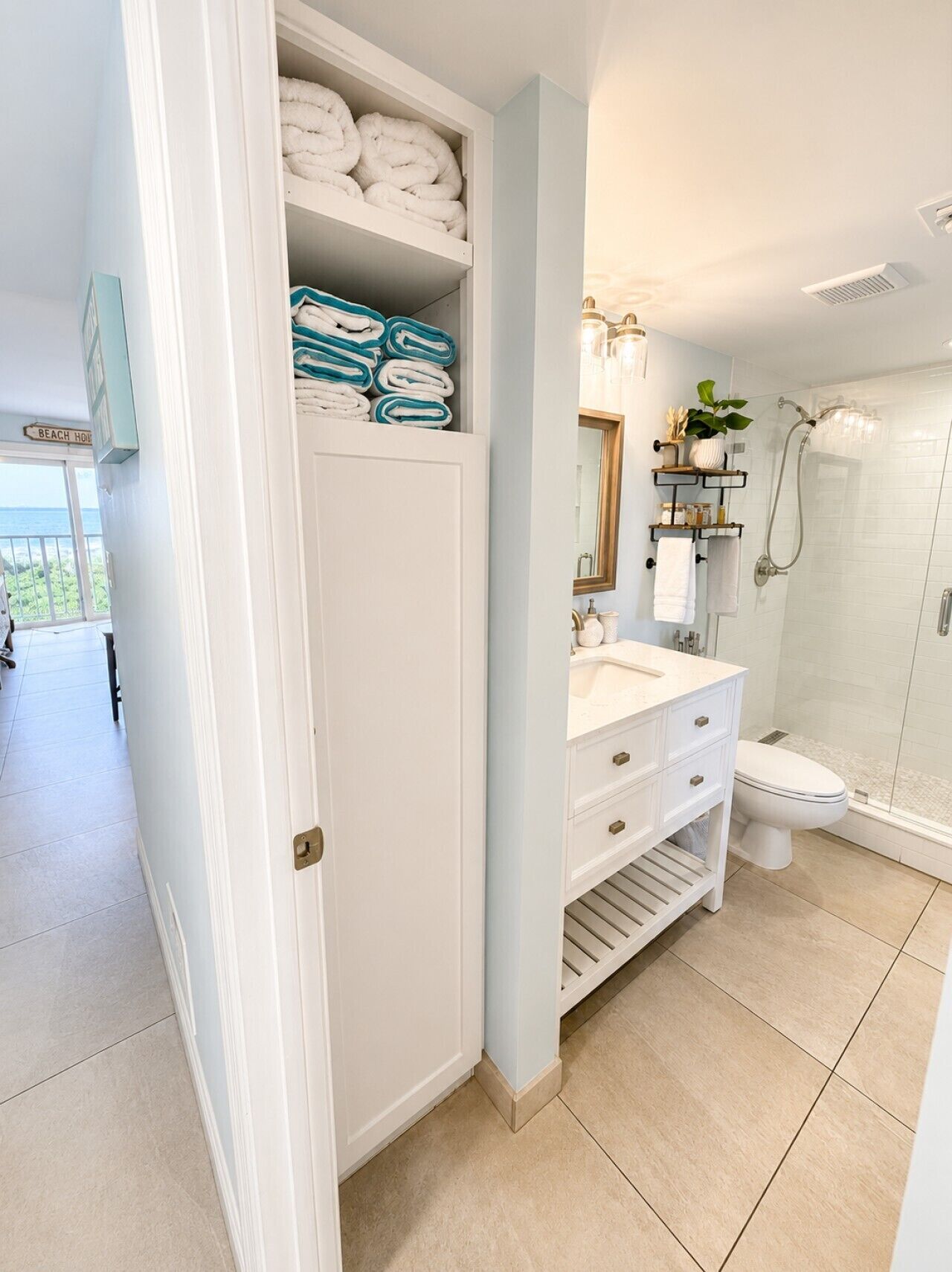 A bathroom with a white vanity, a shower, and a towel rack with folded towels.