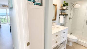 A bathroom with a white vanity, a shower, and a towel rack with folded towels.