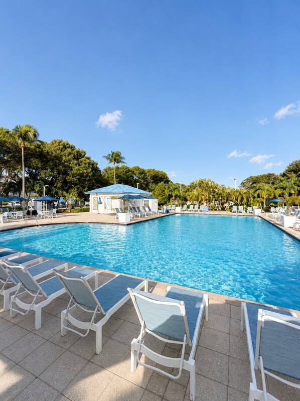 Una piscina con sillones de descanso y un edificio pequeño con techo azul.