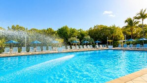 A swimming pool with clear blue water, surrounded by lounge chairs and umbrellas, and a tiled deck area.