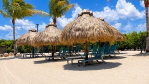 A beach with thatched umbrellas and green lounge chairs.