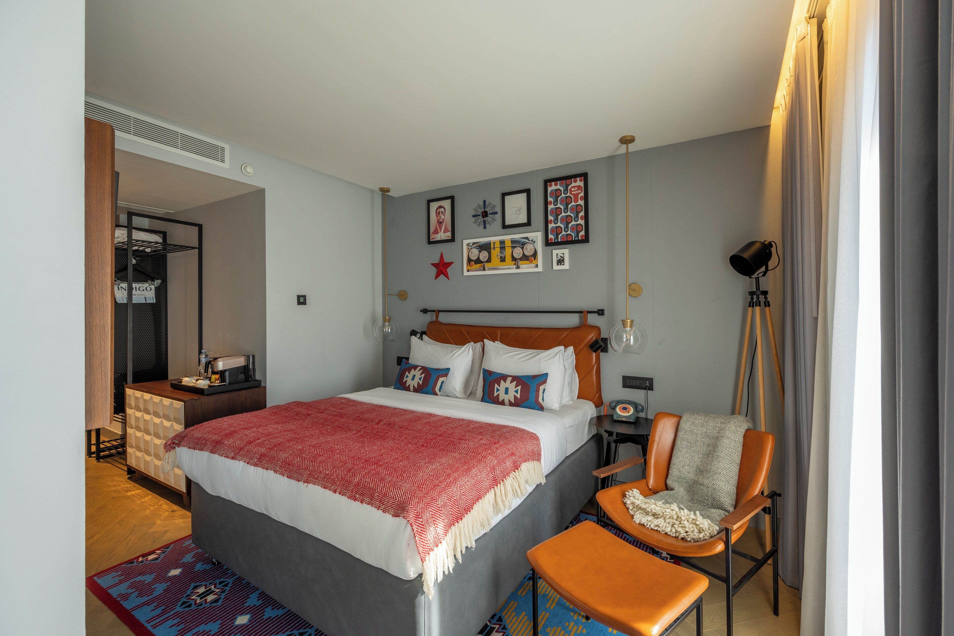 A modern bedroom with a large bed, a chair, a desk, and a wardrobe.