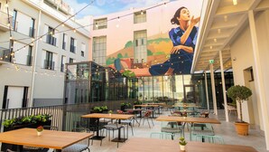 An outdoor patio area with tables and chairs, a mural on the wall, and string lights. - Hotel Indigo Belgrade by IHG (Belgrade)