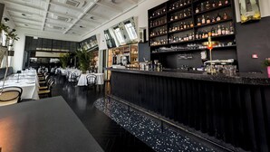 Un restaurant doté d’un bar, de tables dressées pour le service et d’étagères remplies de bouteilles et de verres.