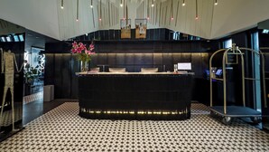 Un hall d’hôtel moderne avec un comptoir d’accueil central, un sol à motifs et des luminaires suspendus.