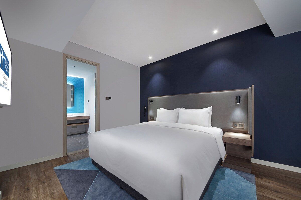 Une chambre d’hôtel moderne avec un grand lit, une table de chevet et une tête de lit intégrée.
