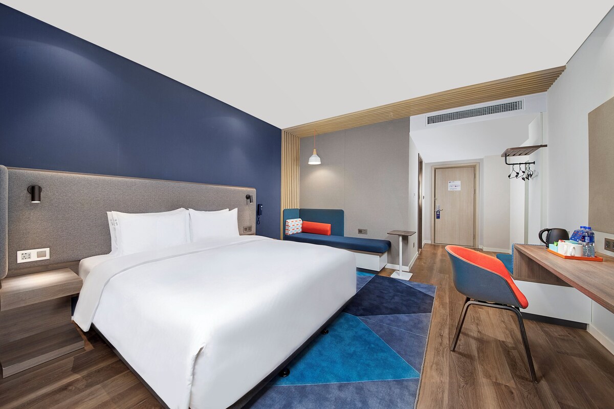 Une chambre d’hôtel moderne dotée d’un grand lit, d’un bureau avec une chaise, d’un petit coin salon et d’une kitchenette.