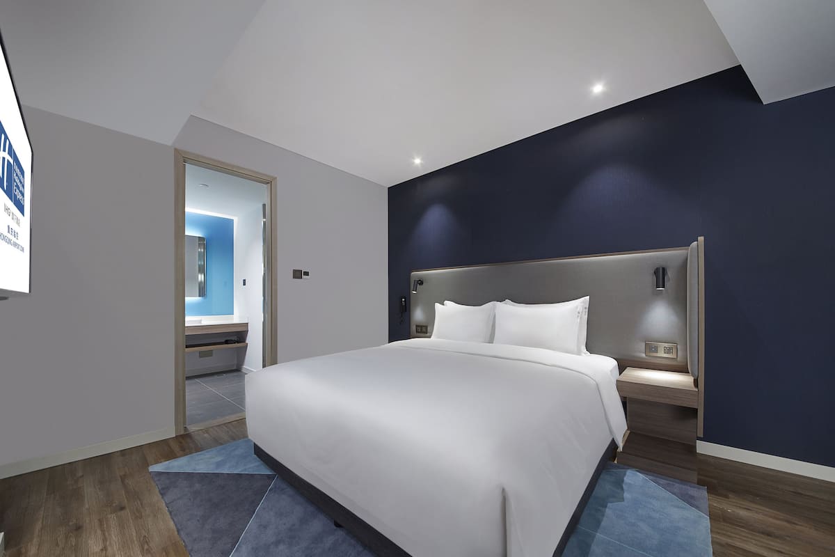 A modern hotel room with a large bed, a nightstand, and a built-in headboard.