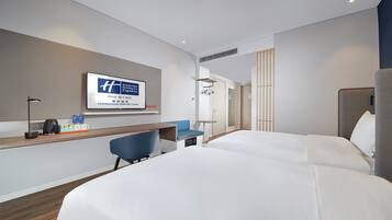 Habitación de hotel con dos camas, un escritorio con silla, un televisor en la pared y una pequeña zona de estar.