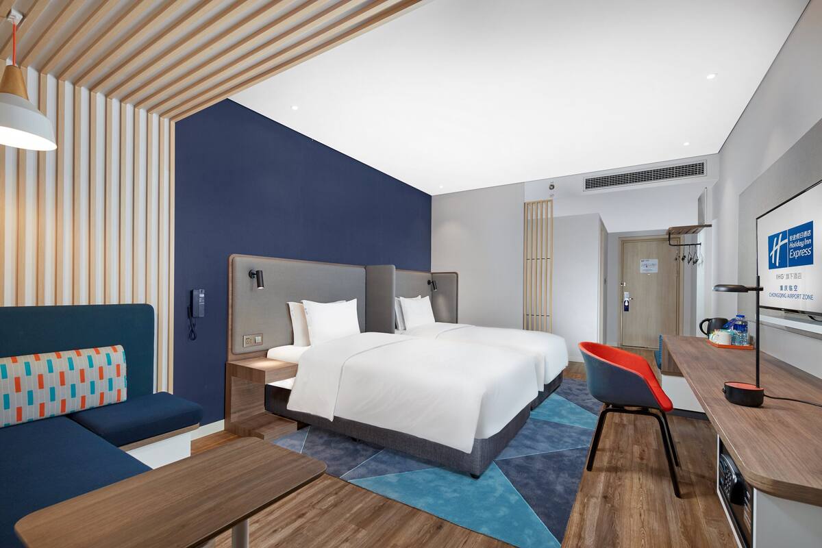 A modern hotel room with a large bed, a sofa, a desk, and a chair.