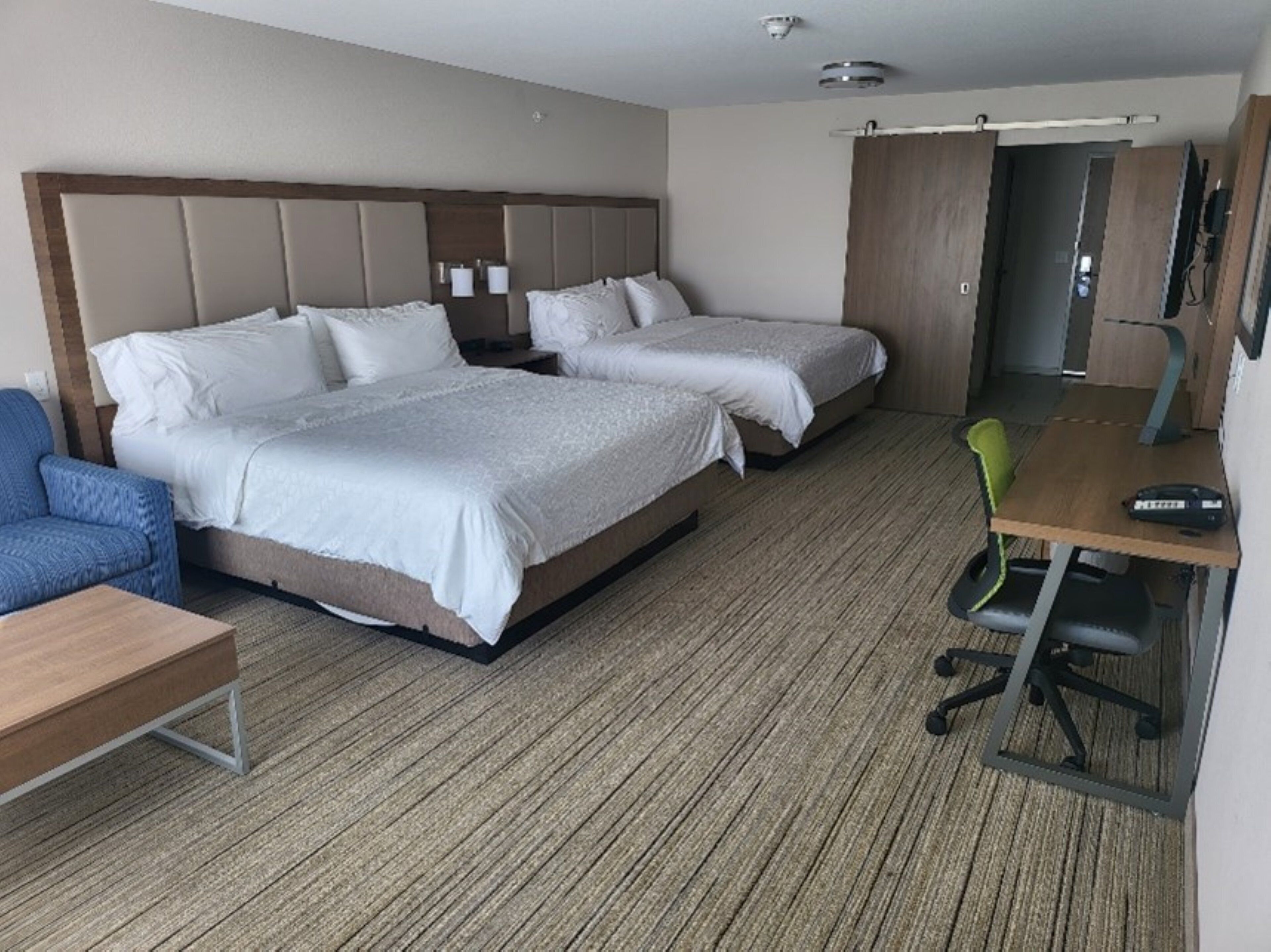 A hotel room with two beds, a desk, a chair, and a television.
