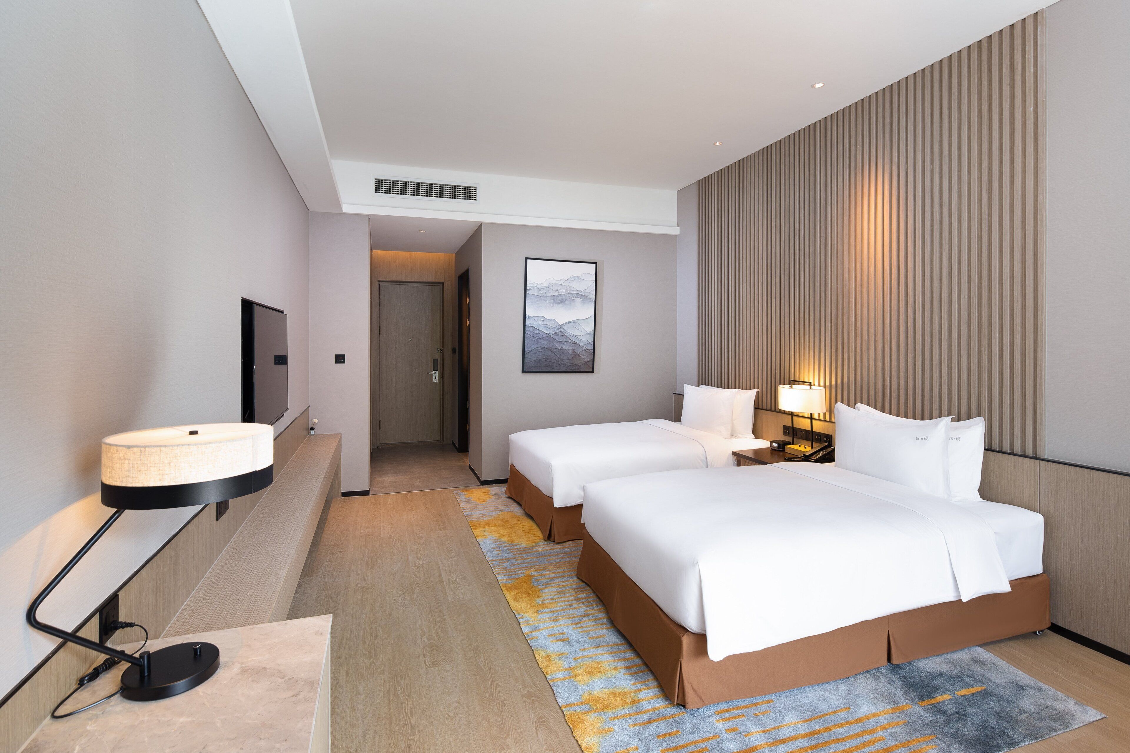 A hotel room with a large bed, bedside tables with lamps, a flat-screen TV mounted on the wall, and a wooden floor.