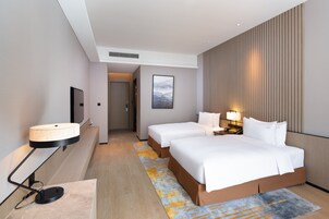A hotel room with a large bed, bedside tables with lamps, a flat-screen TV mounted on the wall, and a wooden floor.