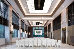 A conference room with rows of white chairs, a large screen at the front, and a high ceiling with recessed lighting.