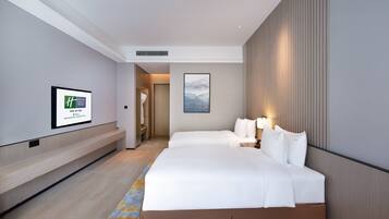 A hotel room with two beds, a large window, a mounted artwork, and a visible bathroom door.