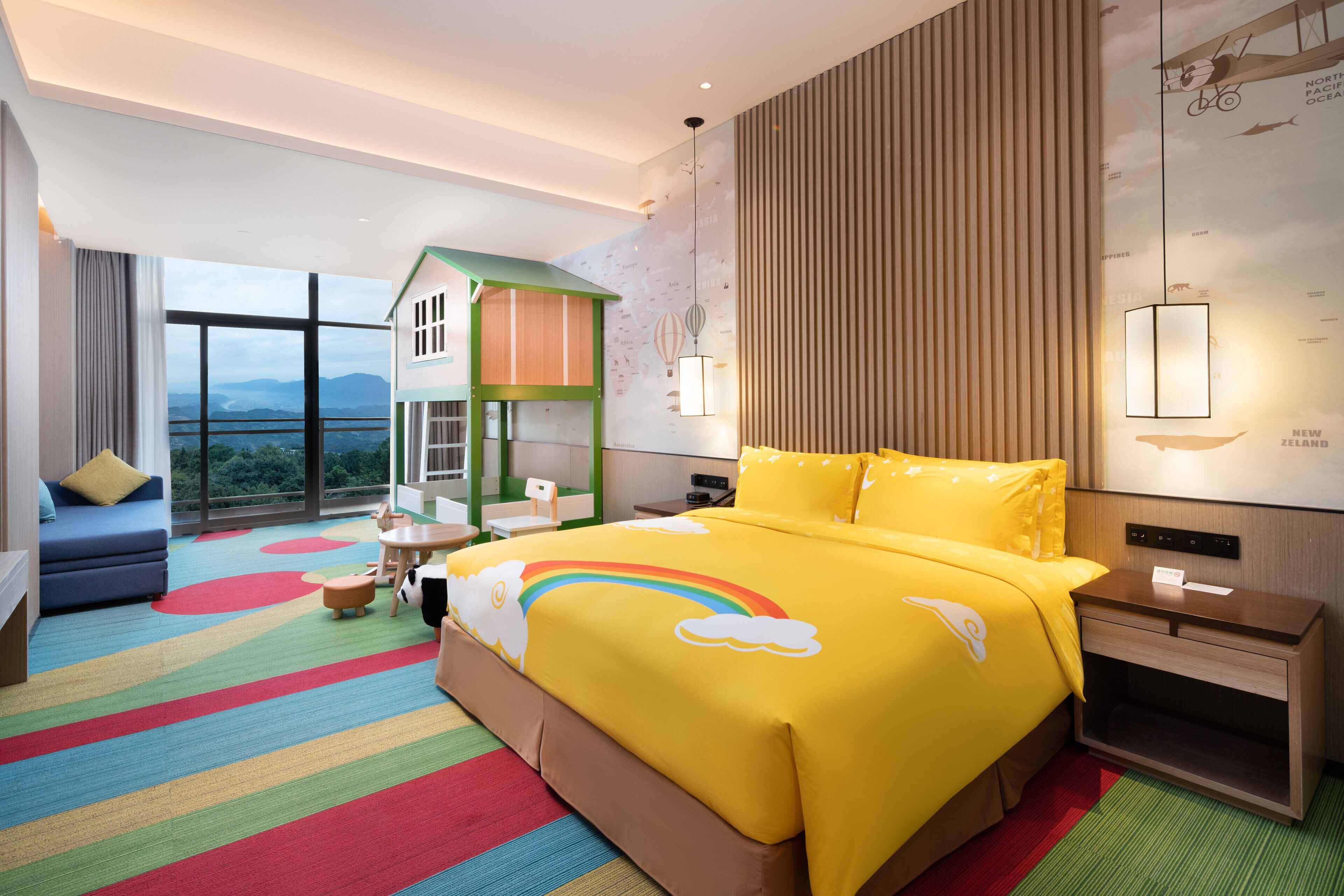 Une chambre d’hôtel avec un grand lit, un petit espace de jeux, une vue sur les montagnes et une moquette colorée.