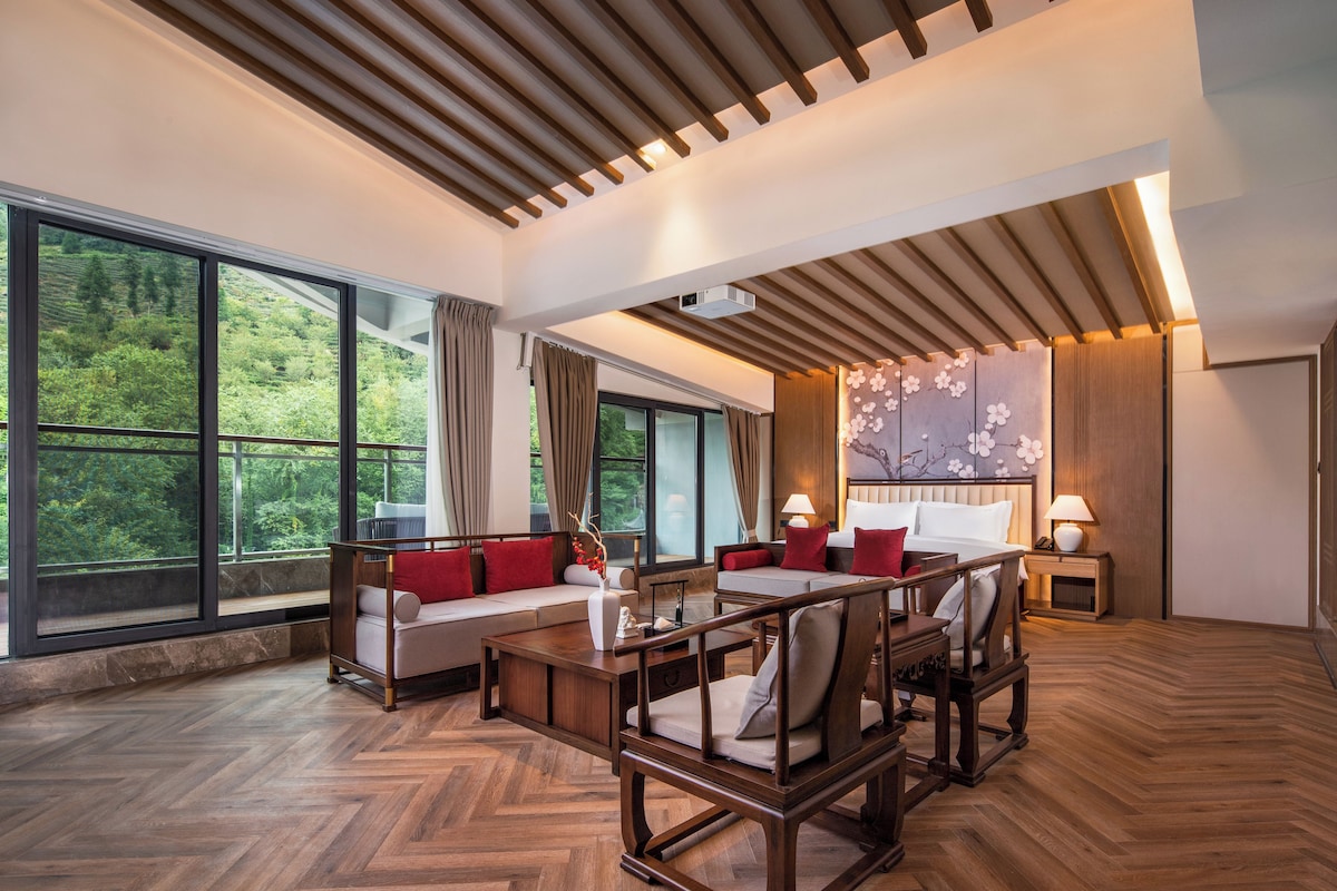 Une pièce spacieuse dotée d’une grande fenêtre, d’un plafond en bois et d’un coin salon avec un canapé et des fauteuils.
