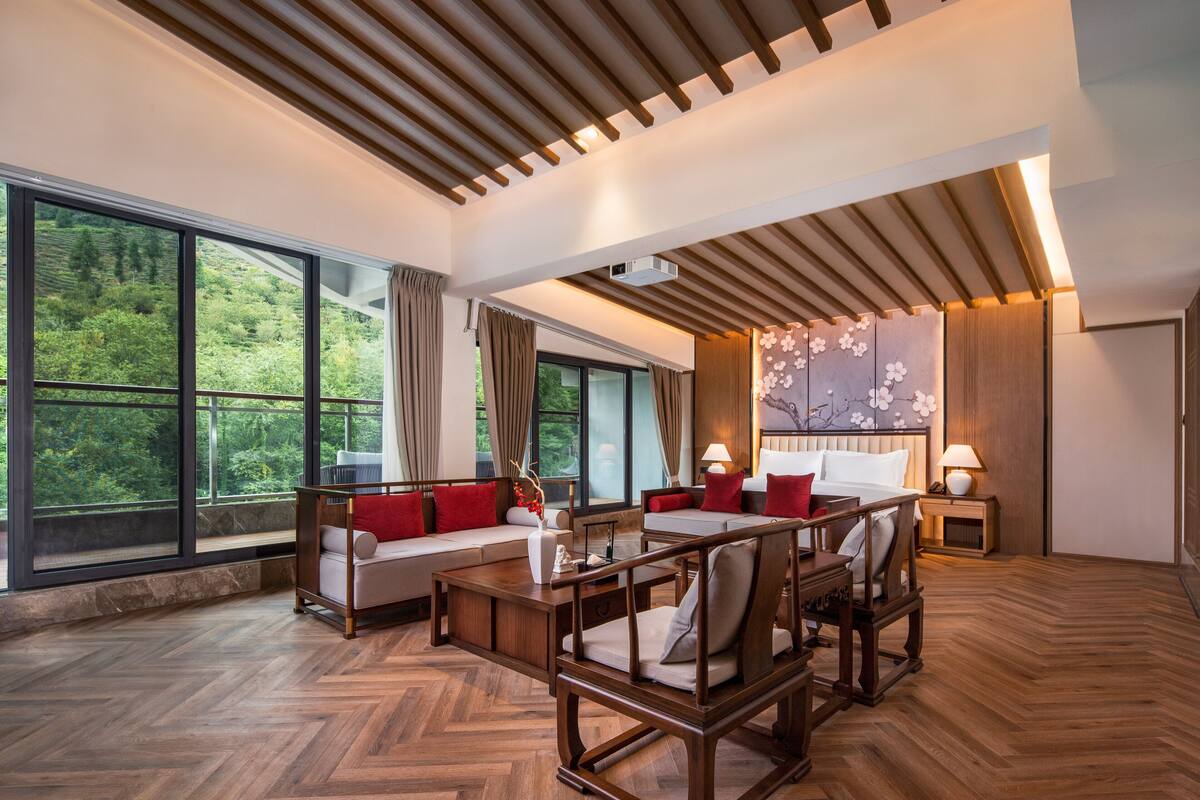 A spacious room with a large window, a wooden ceiling, and a seating area with a sofa and chairs.