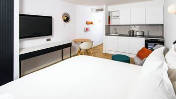 Una habitación de hotel moderna con una cama grande, un televisor montado en la pared, una mesita redonda y una kitchenette con un fregadero y un tostador.
