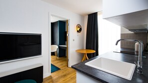 A modern kitchen with a large sink, a dining area with a table and chairs, and a TV mounted on the wall. - Staybridge Suites Cardiff by IHG (Cardiff)