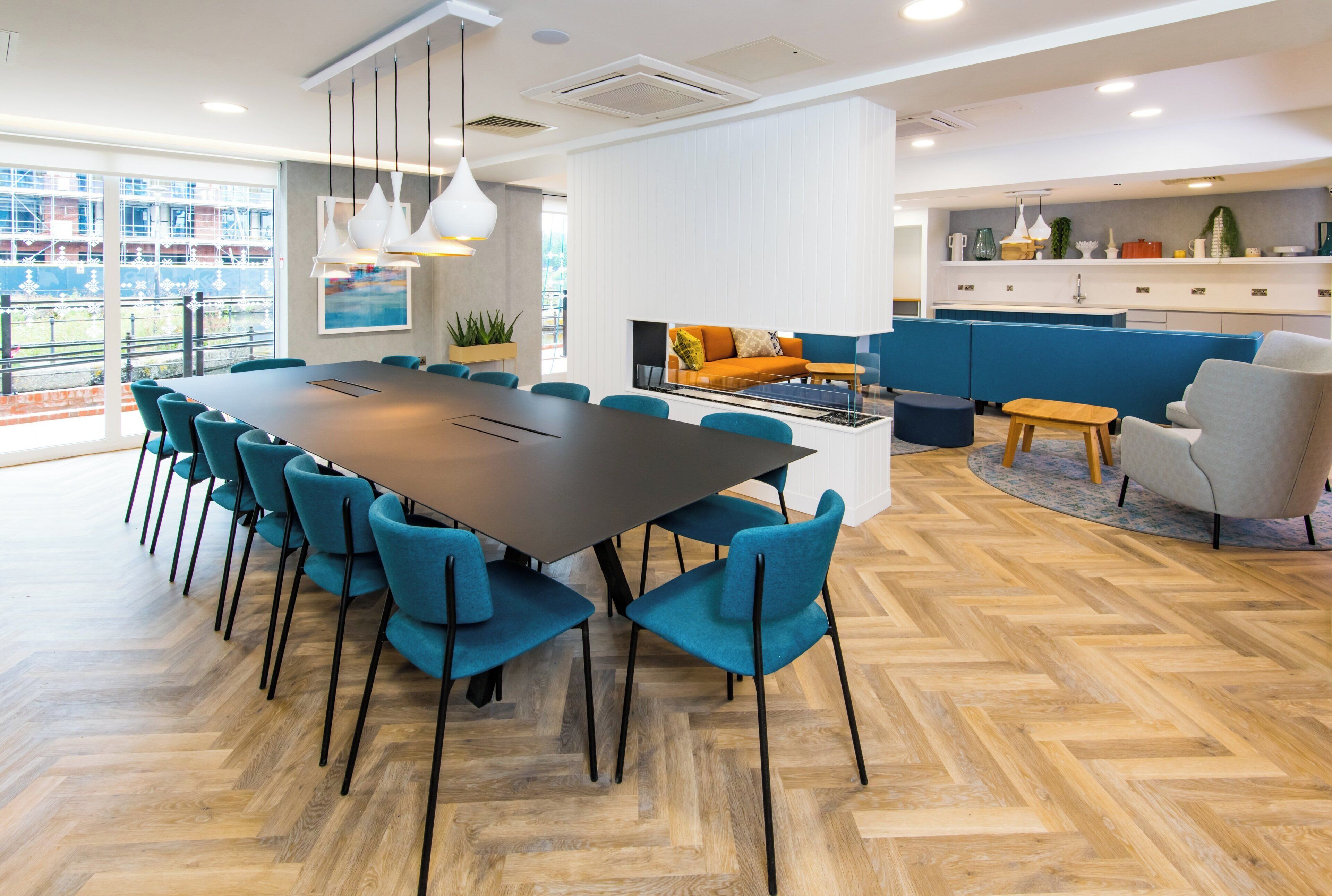Un espace repas moderne avec une grande table, des chaises de couleur turquoise et un parquet en bois disposé en chevrons.