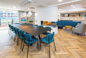 A modern dining area with a large table, teal chairs, and a herringbone wood floor. - Staybridge Suites Cardiff by IHG (Cardiff)