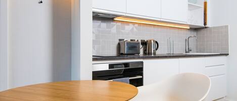 A modern kitchen with white cabinetry, a round wooden table, and two white chairs.