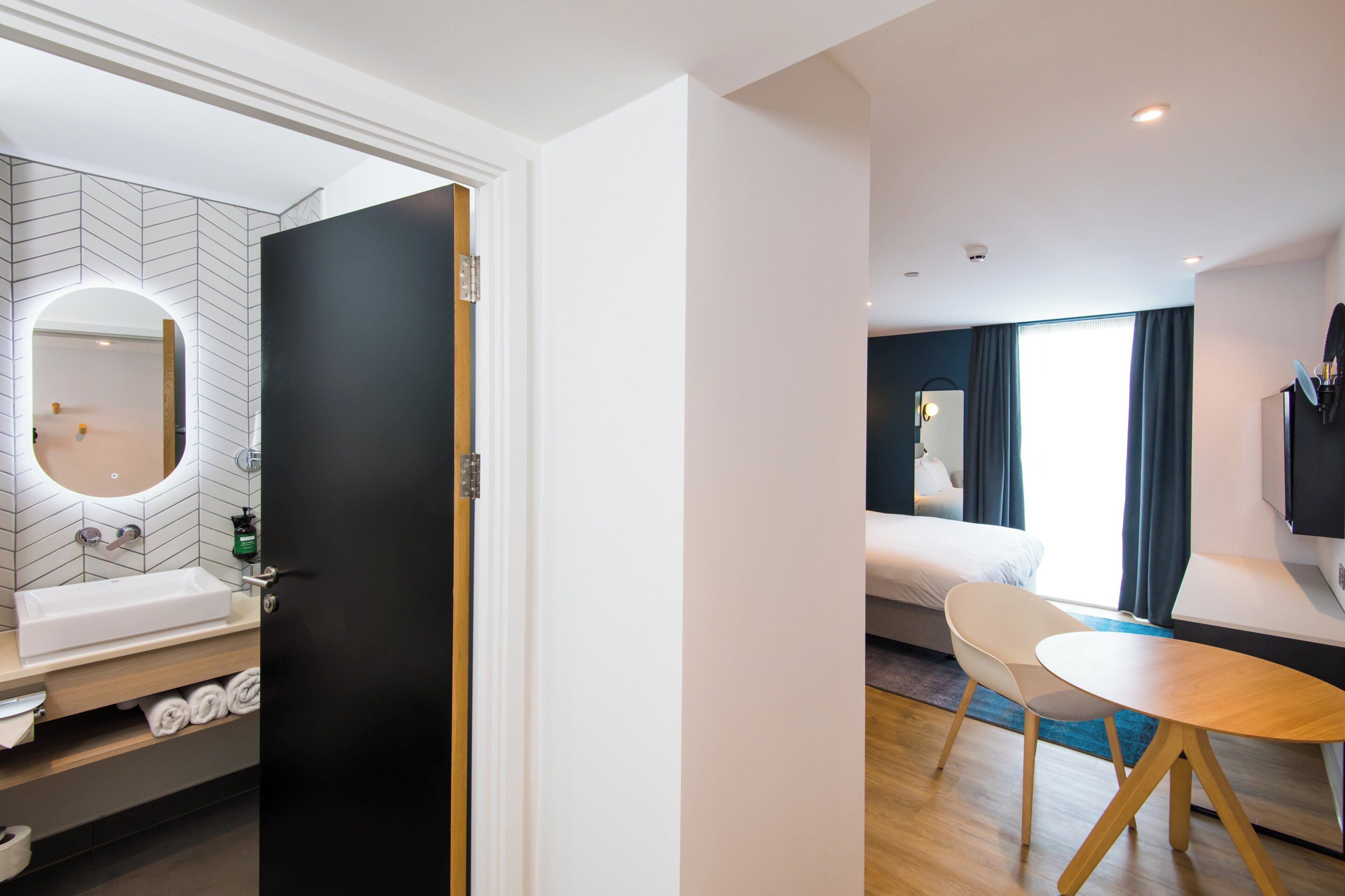A hotel room with a bathroom, a bed, a TV, and a dining area.