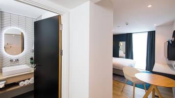 Habitación de hotel con baño, cama, televisor y zona de comedor.