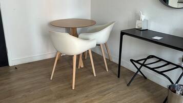 Quarto moderno com uma mesa redonda, duas cadeiras brancas, uma escrivaninha de metal preto e uma lixeira.