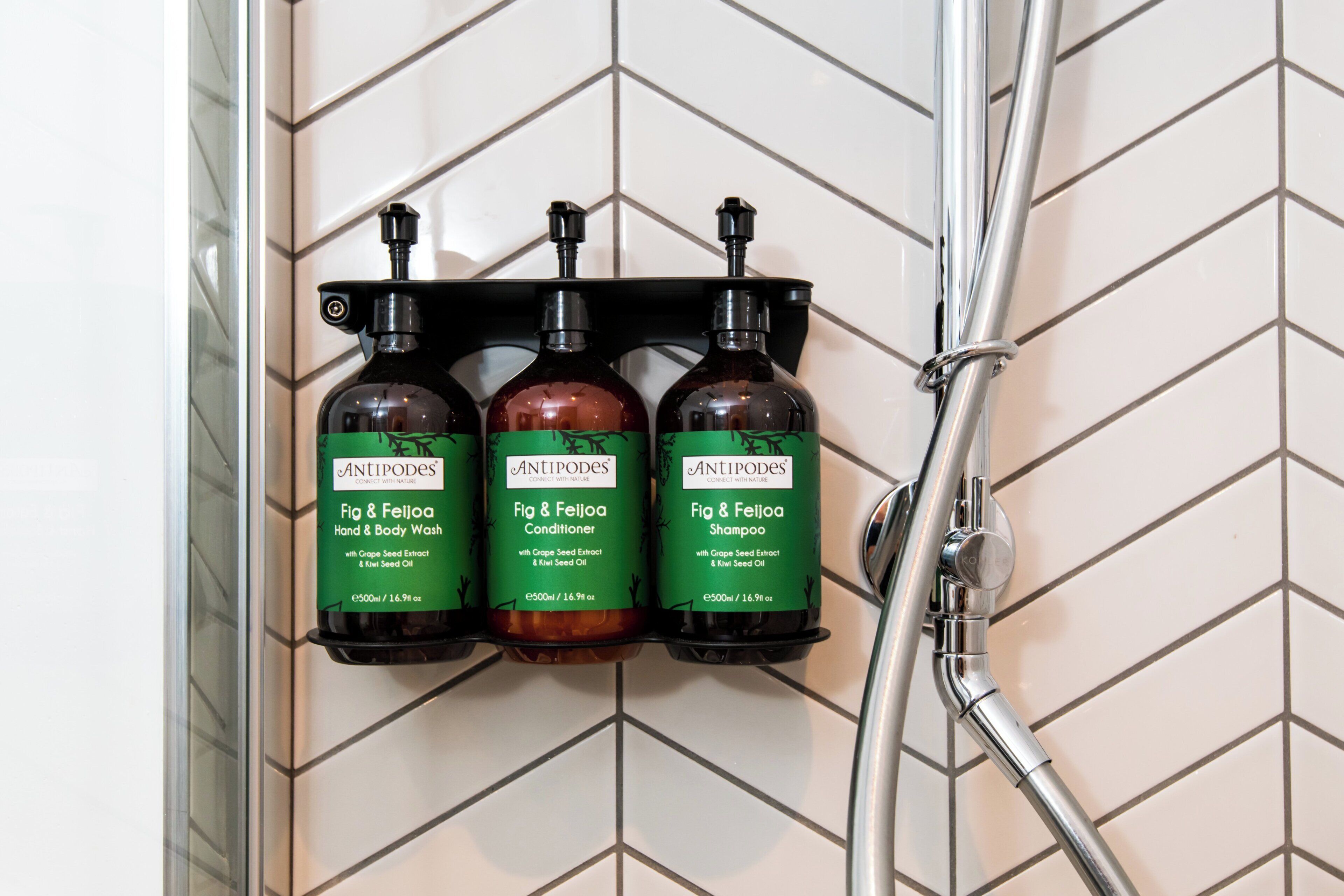 Une salle de bain avec une douche et trois flacons de produits de la marque Antipodes.