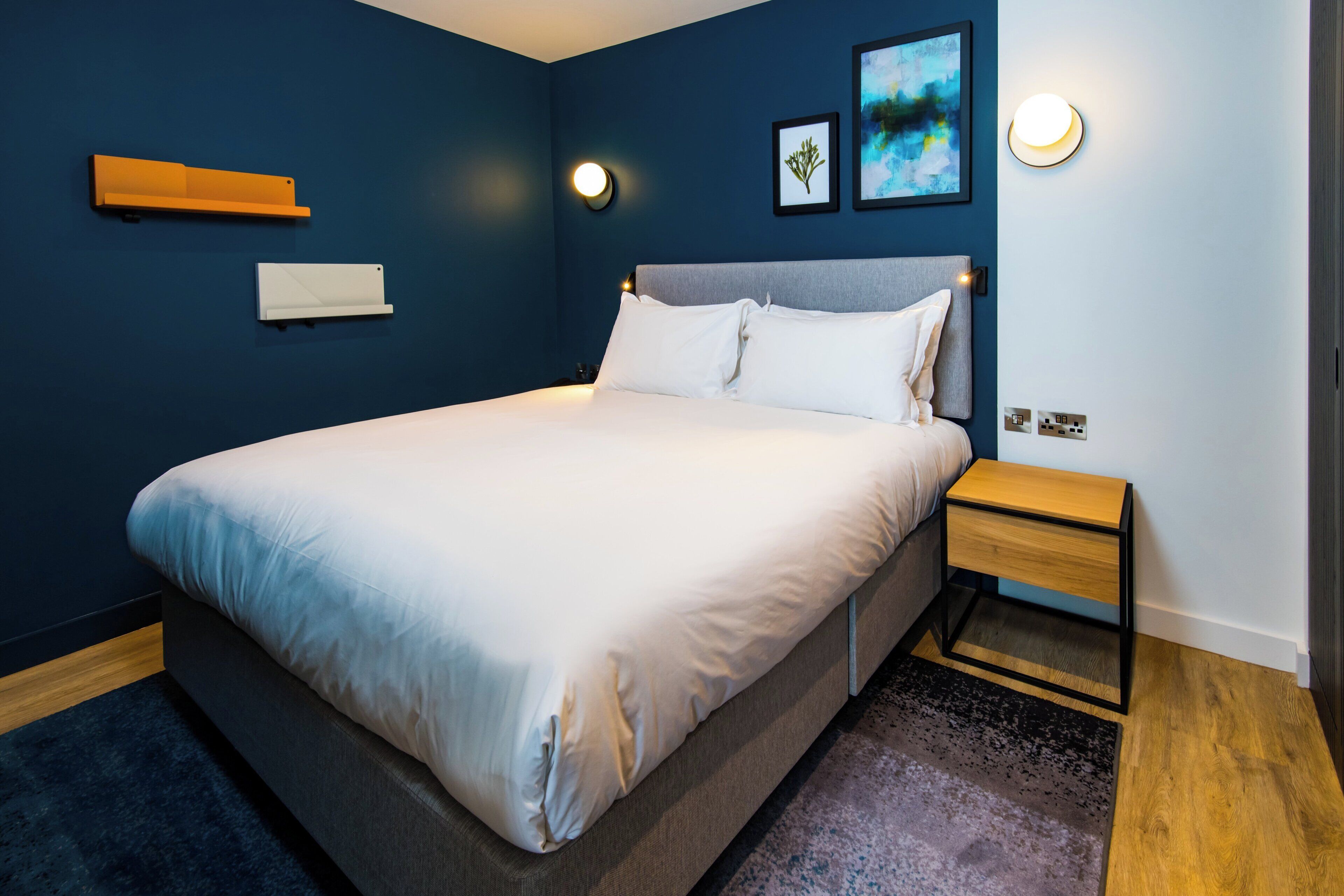 Quarto moderno com cama grande, mesa de cabeceira e luminárias fixadas na parede.