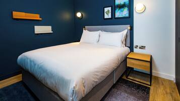 A modern bedroom with a large bed, bedside table, and wall-mounted light fixtures.