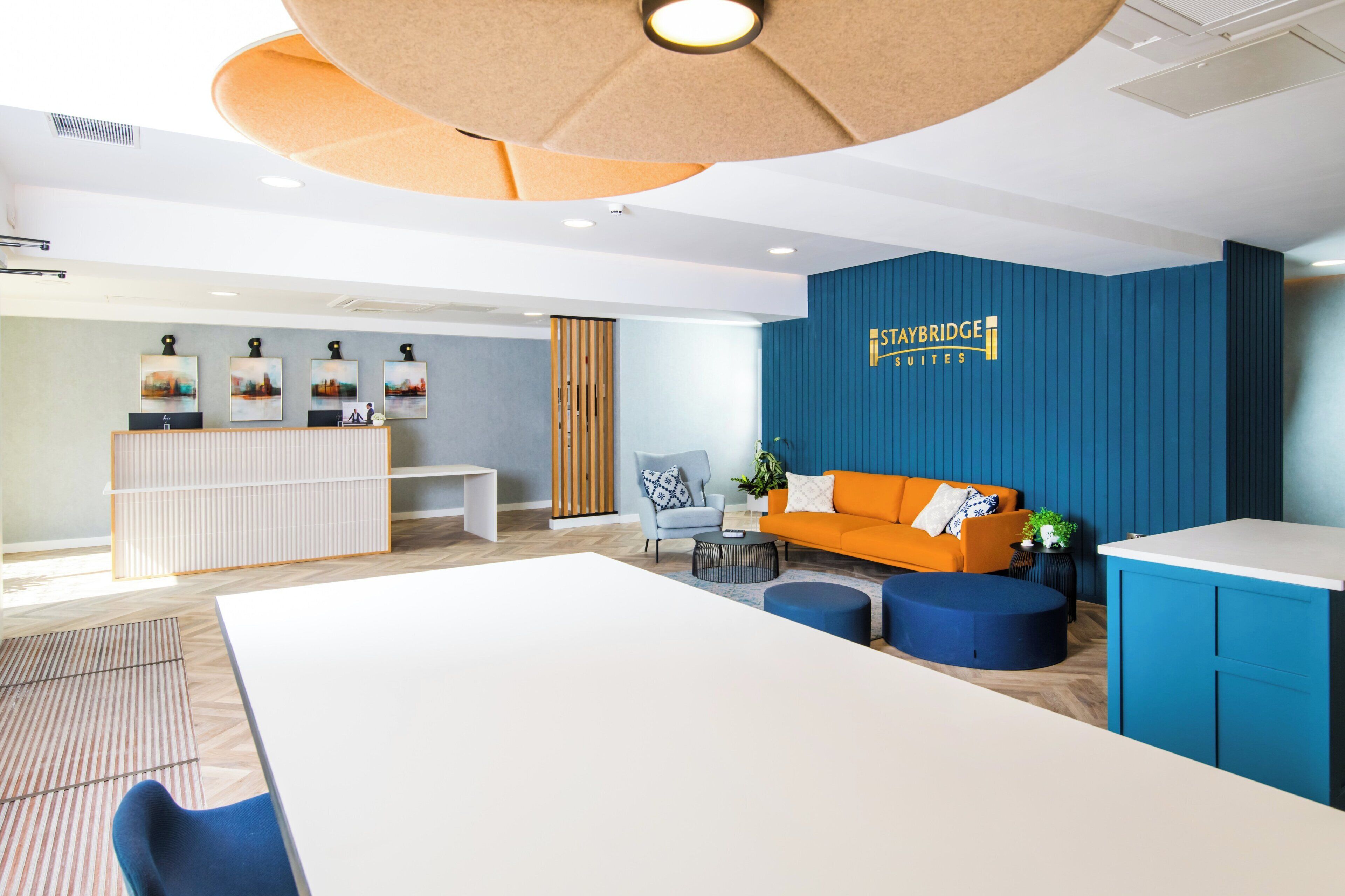 A hotel reception area with a reception desk, seating area with a sofa and chairs, and a wall with the hotel name.
