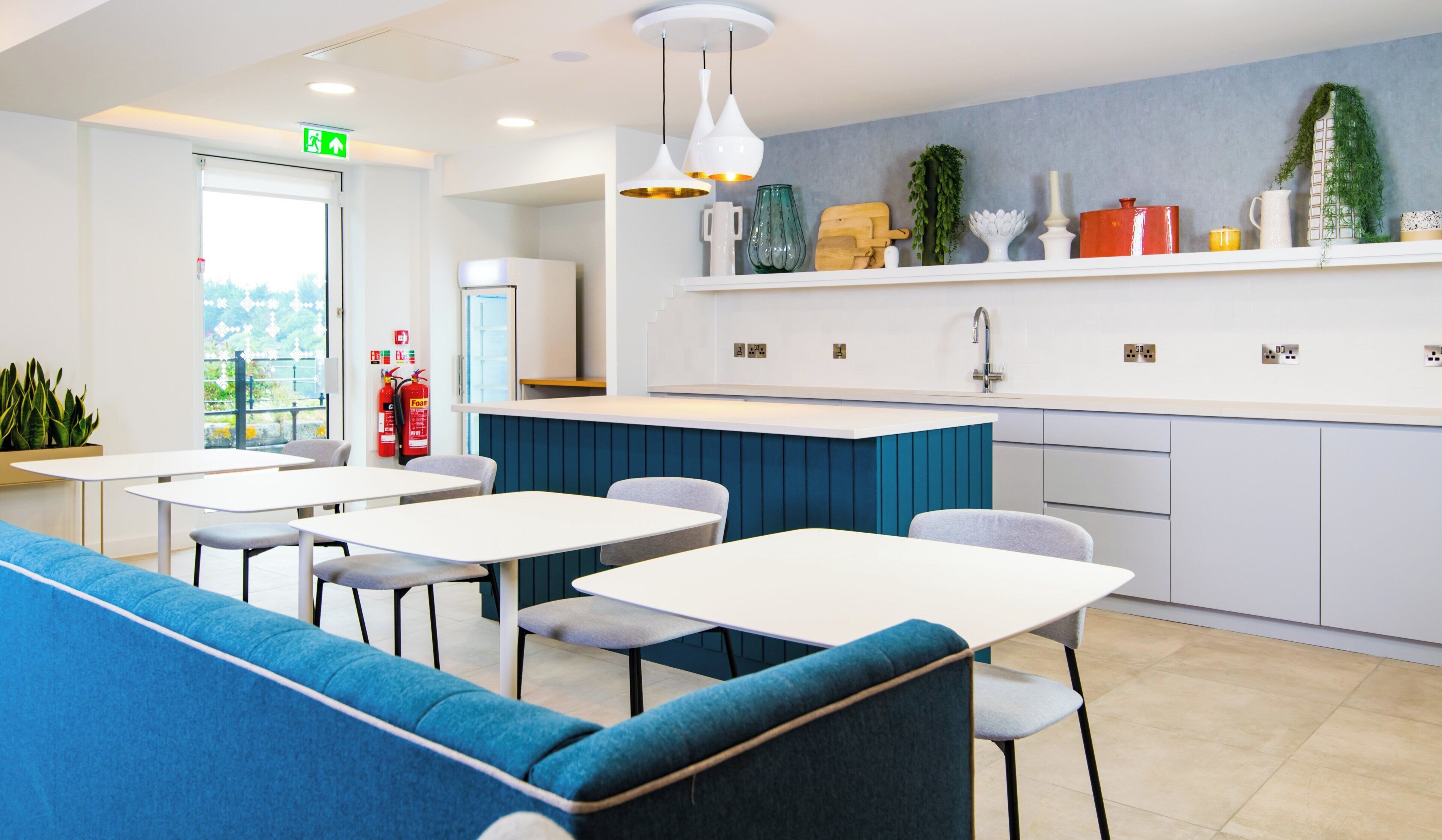 Un espace repas moderne avec des tables et des chaises, un comptoir de cuisine et un mur d’accent bleu.