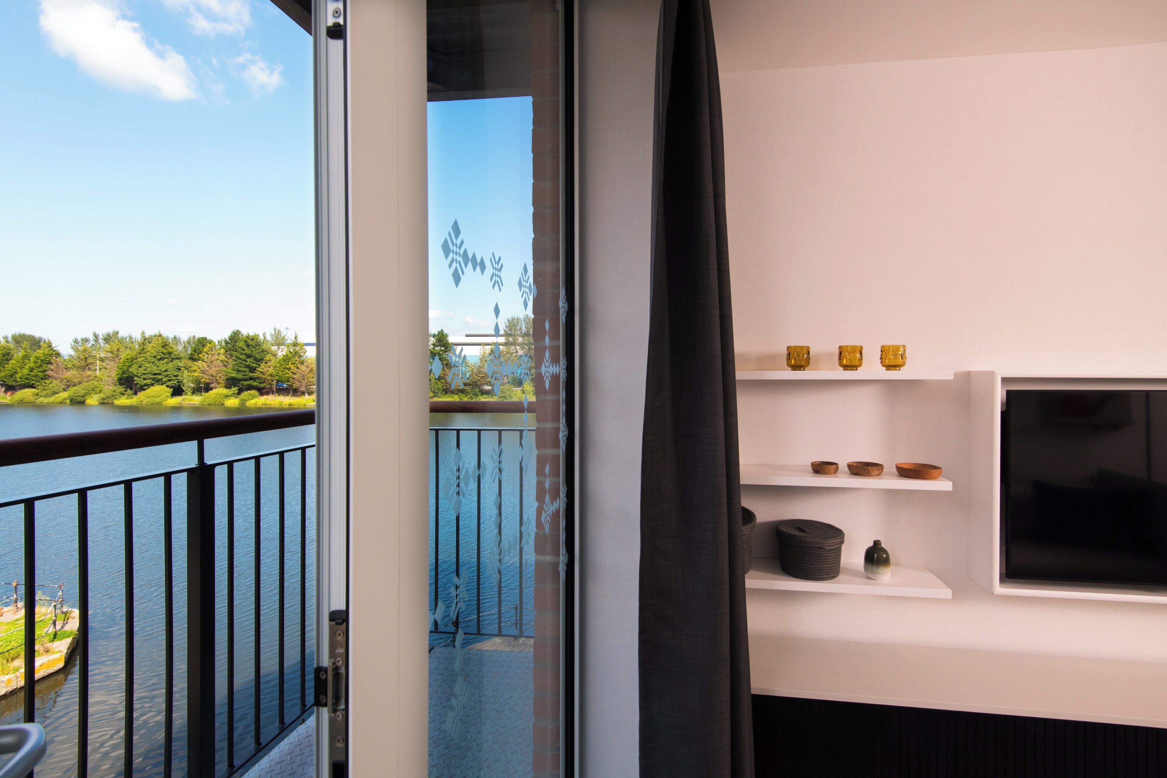 Quarto com vista para um lago, varanda com guarda-corpo e prateleira branca com objetos decorativos.