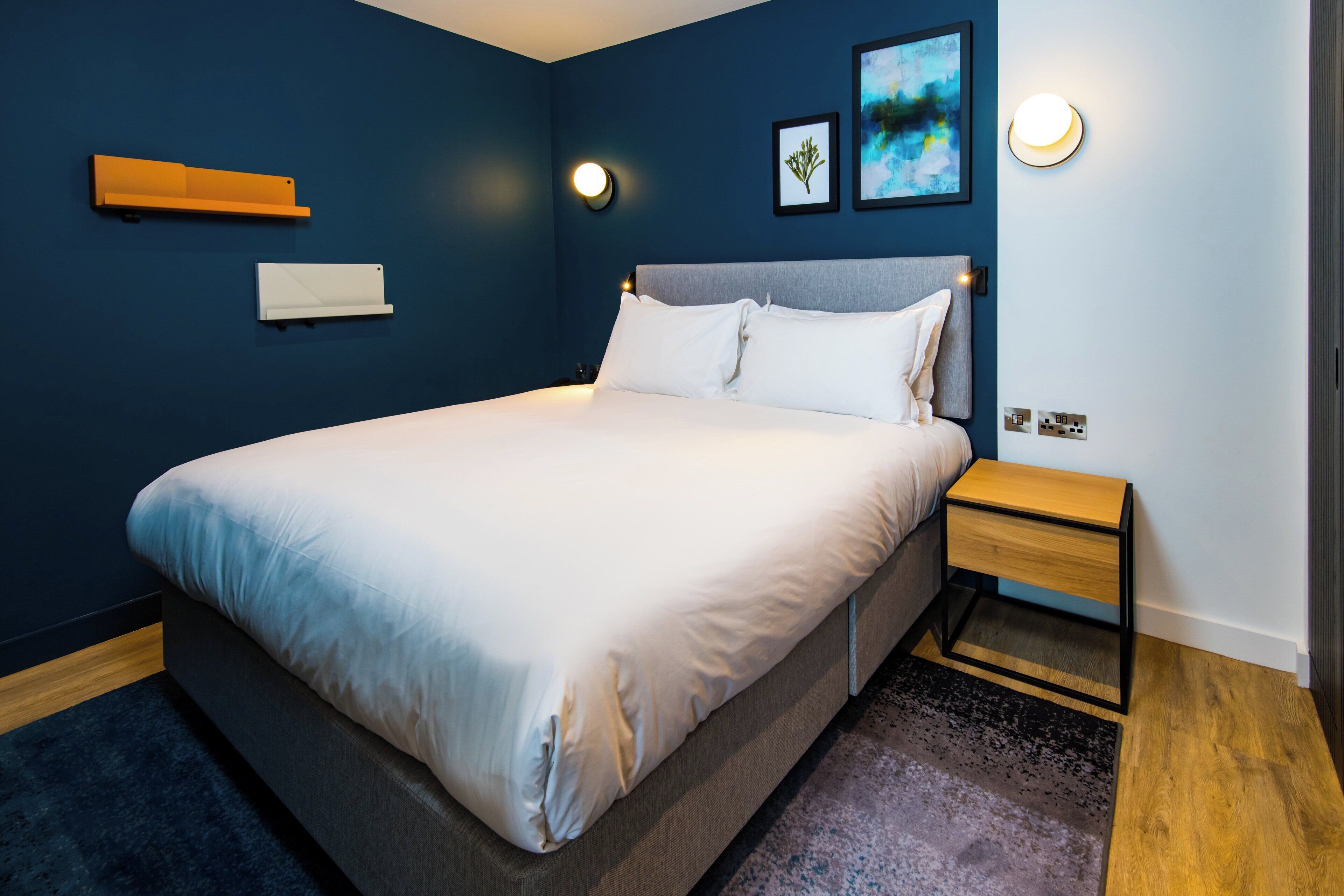 A modern bedroom with a large bed, a bedside table, and a wall-mounted shelf.
