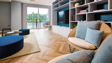 A modern living room with a large TV, comfortable seating, and a view of a river.