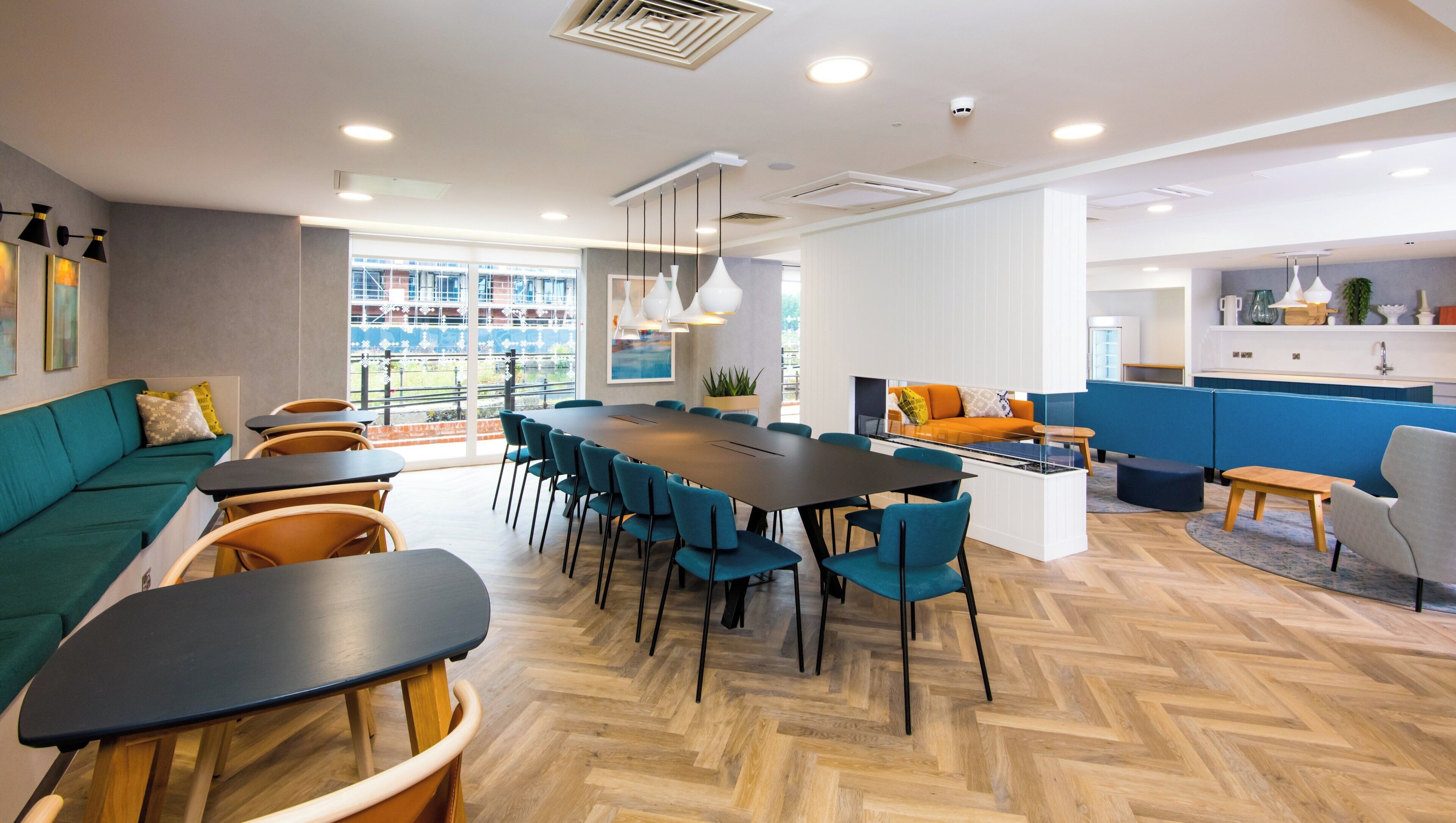 Un espace de détente moderne avec une longue table, plusieurs chaises, un canapé et, au fond, un coin cuisine.