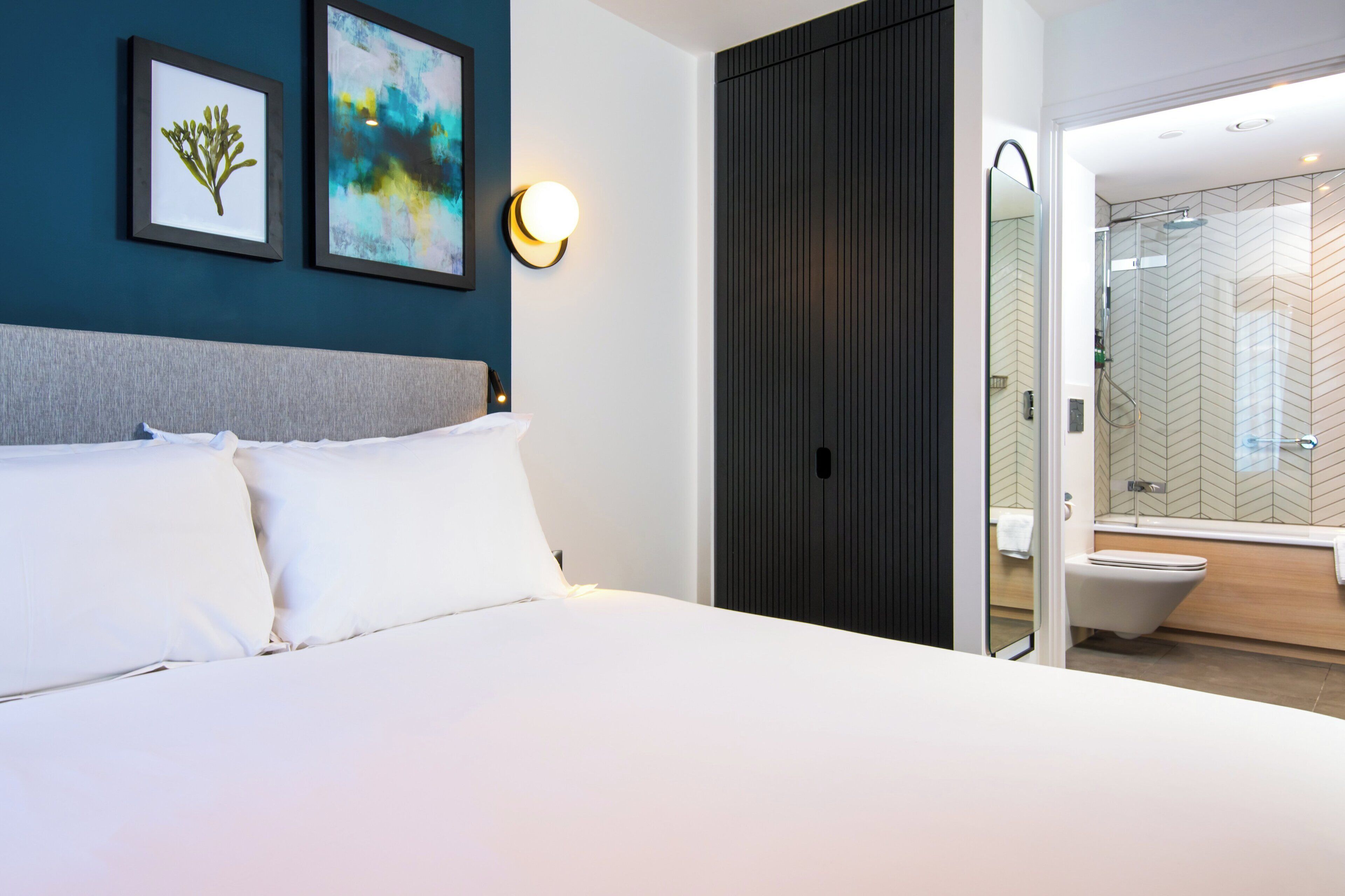 A hotel room with a bed, a wall-mounted light, and a bathroom visible through an open door.