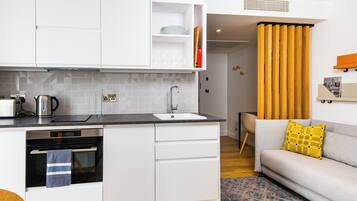 Una cocina compacta con muebles blancos, horno integrado y lavamanos.