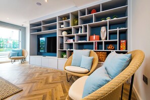 A modern living room with a large TV, wicker chairs, and a built-in shelving unit. - Staybridge Suites Cardiff by IHG (Cardiff)